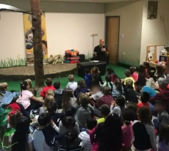 Wildlife educator presenting to a large group of seated children indoors