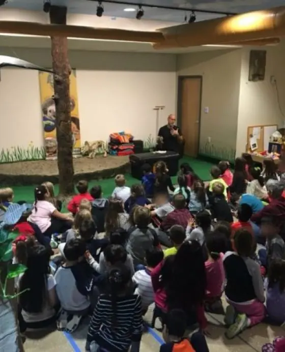Wildlife educator presenting to a large group of seated children indoors